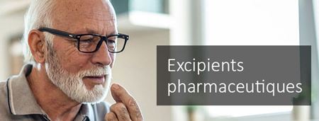 Un homme âgé aux cheveux et à la barbe blancs, portant des lunettes, prend un comprimé pharmaceutique avec un verre d’eau.
